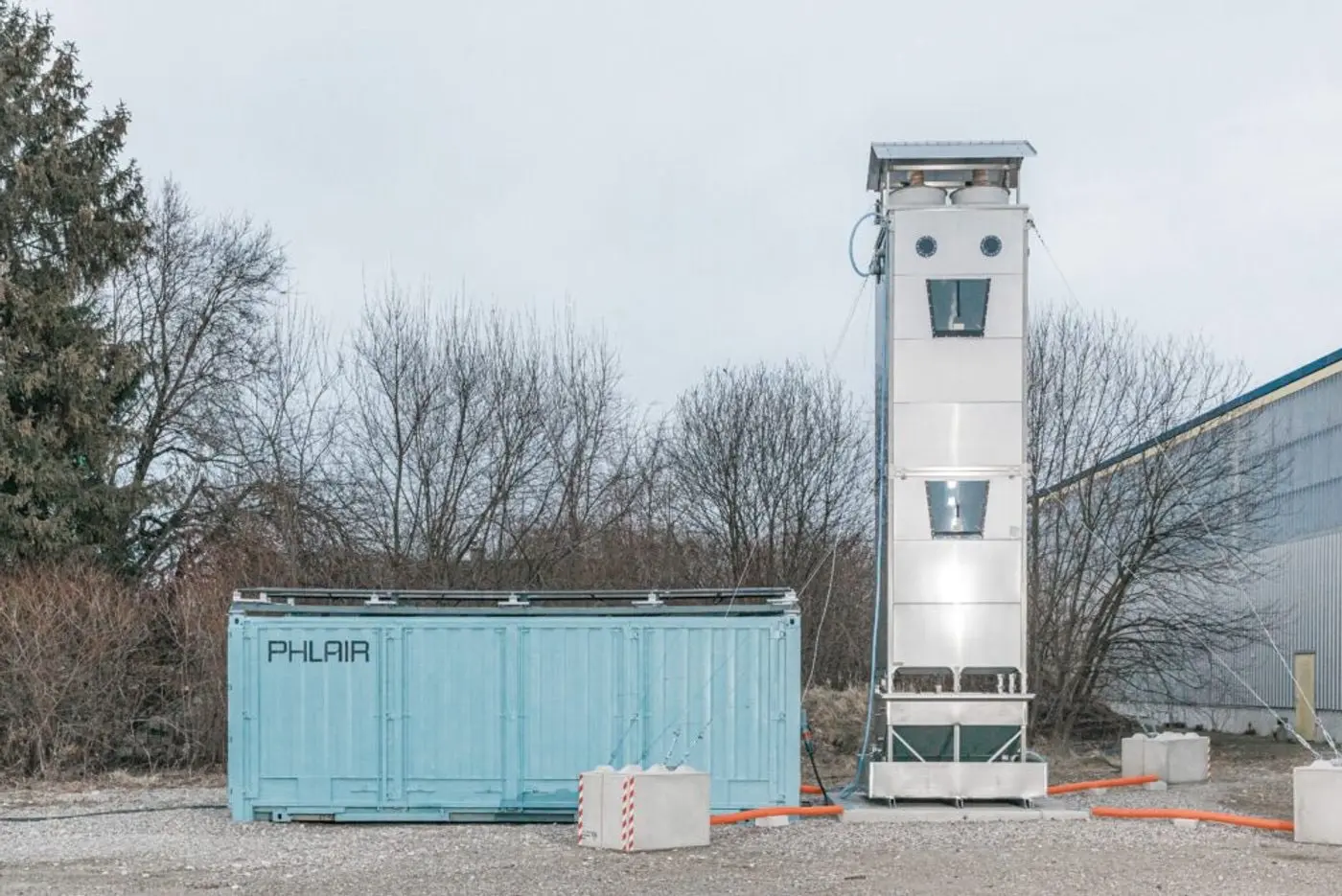 Phlair's pilot plant: a light-blue container unit beside a tall white capture tower on a gravel yard